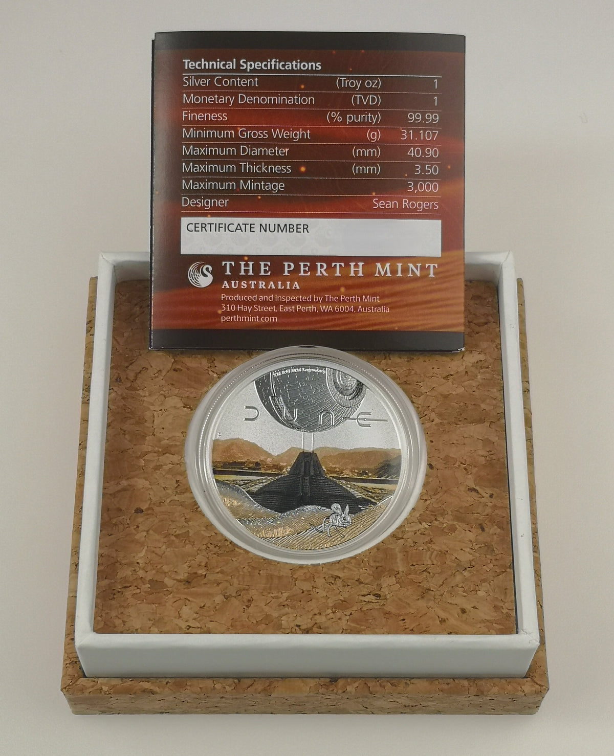 A Perth Mint Australia Dune silver coin in a clear protective capsule, displayed inside a cork-lined presentation box with a white insert. A technical specification card is placed above the coin.